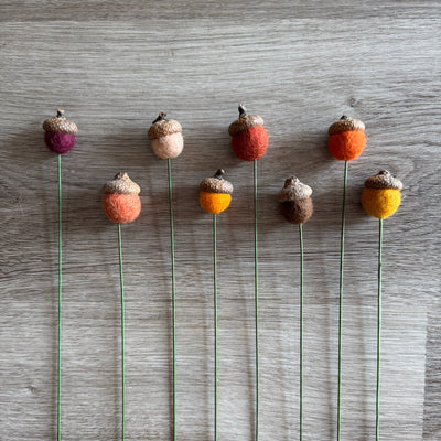 Decorative acorn-shaped flowers on green stems against a wooden background